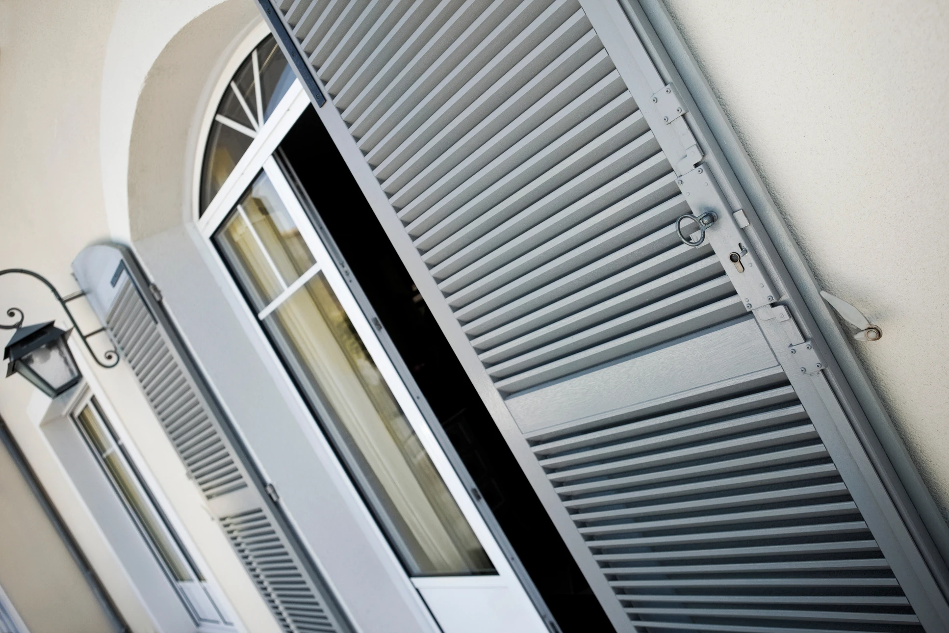 Façade extérieure d'habitation avec fenêtre cintrée ouverte et volets battants en aluminium blanc à lames orientables