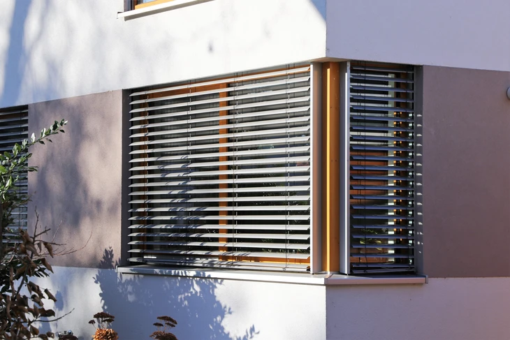 Façade extérieure d'un bâtiment moderne avec deux fenêtres équipées de stores vénitiens extérieurs en aluminium
