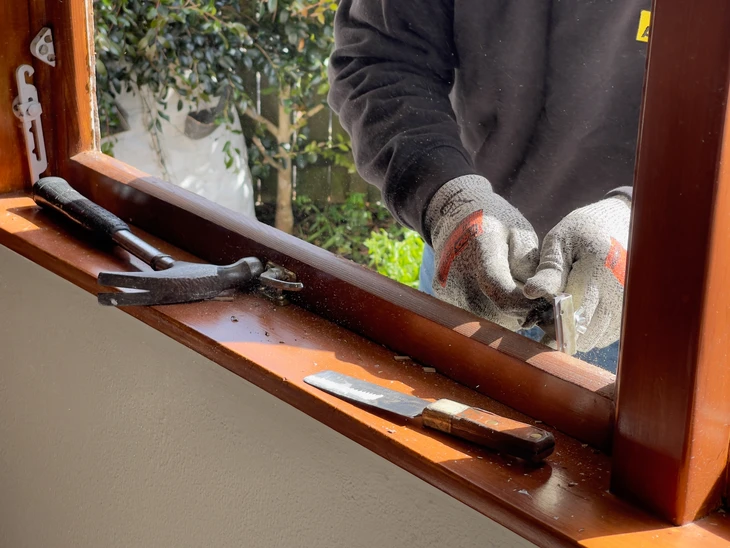 Artisan menuisier travaillant sur une fenêtre en bois, utilisant un rabot manuel pour ajuster le châssis