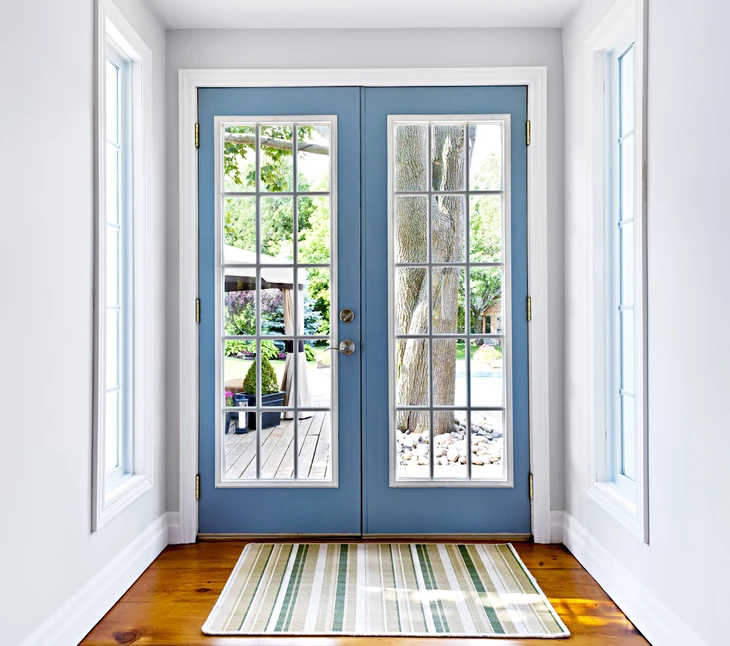 Intérieur résidentiel avec porte-fenêtre double battant bleue ouvrant sur terrasse et jardin