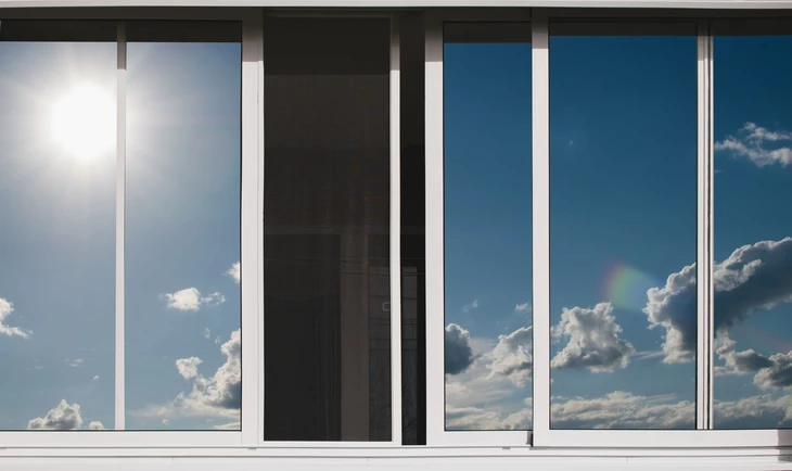 Intérieur moderne avec grande baie vitrée donnant sur ciel bleu nuageux, soleil éclatant visible