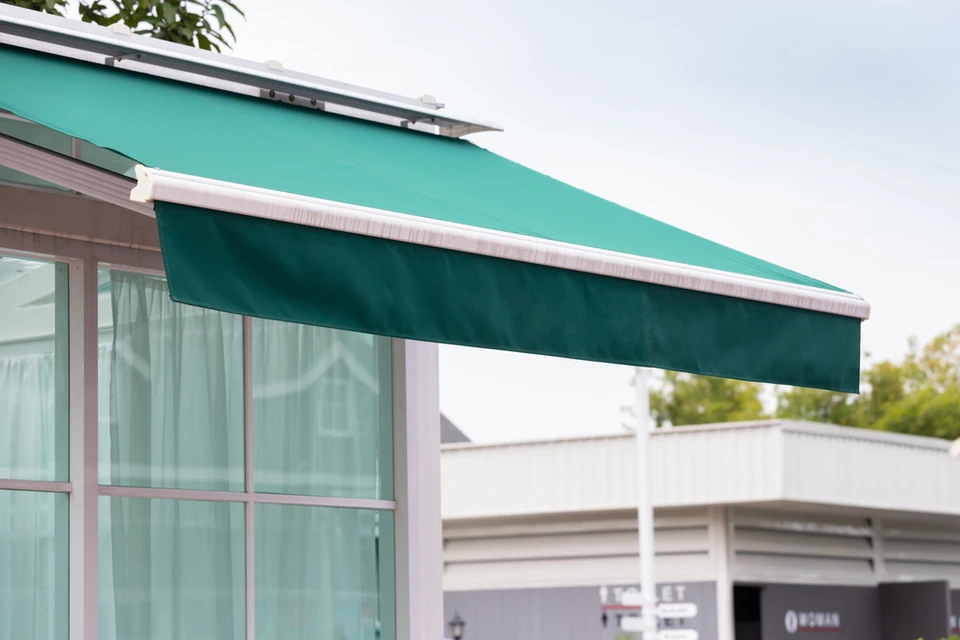 Scène extérieure résidentielle avec store banne vert émeraude déployé au-dessus d'une baie vitrée