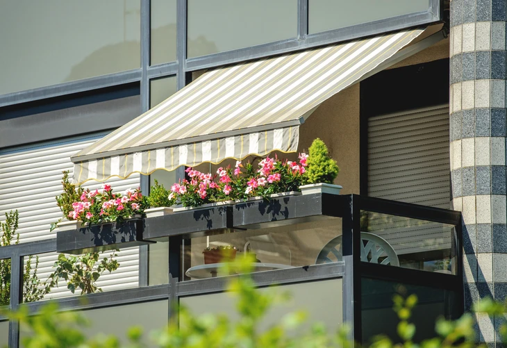 Balcon d'appartement moderne avec store banne rayé beige et blanc déployé pour l'ombrage