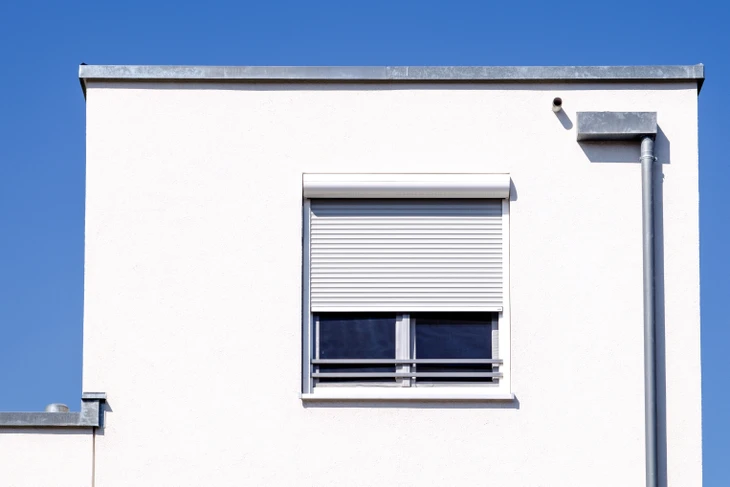 Façade de bâtiment moderne avec volet roulant électrique blanc partiellement fermé sur fenêtre à double vitrage
