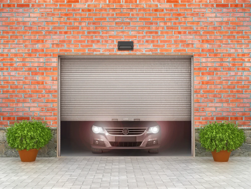 Garage résidentiel avec porte sectionnelle entrouverte laissant voir une voiture aux phares allumés