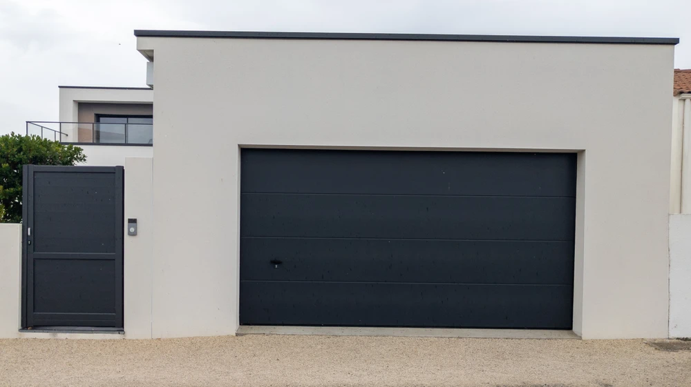 Façade extérieure de maison contemporaine avec porte de garage sectionnelle anthracite à panneaux horizontaux et portillon assorti