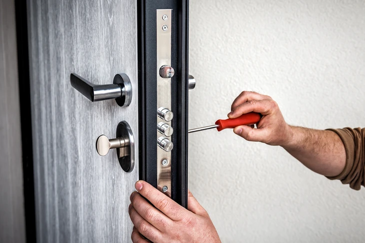 Un bricoleur professionnel répare l'écluse de la porte d'entrée métallique, Un homme réparant l'écluse avec tournevis