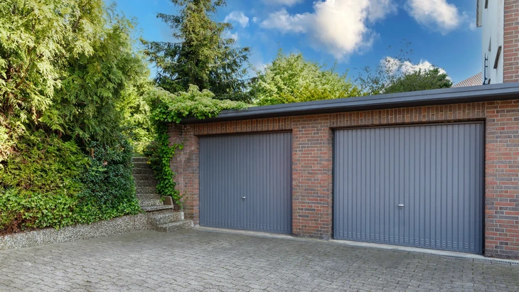 Garage moderne dans maison de briques résidentielle pour voitures avec volets à rouleaux gris sur portes