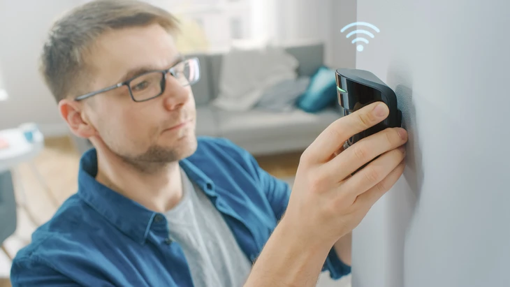 Un homme portant des lunettes installe un dispositif de sécurité connecté sur un mur intérieur