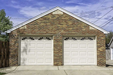 Façade extérieure d'un garage résidentiel à deux places avec portes sectionnelles blanches à panneaux rectangulaires et hublots décoratifs semi-circulaires