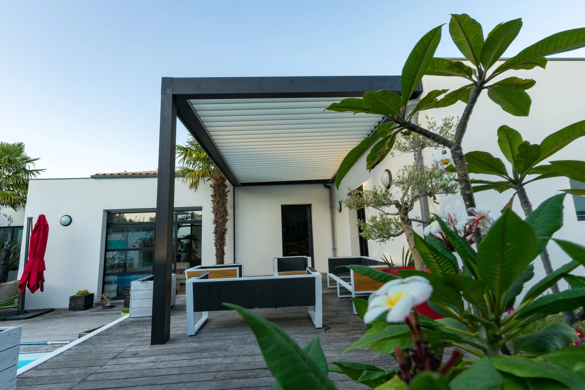 Terrasse moderne avec pergola bioclimatique à lames orientables, mobilier contemporain noir et blanc sur terrasse bois