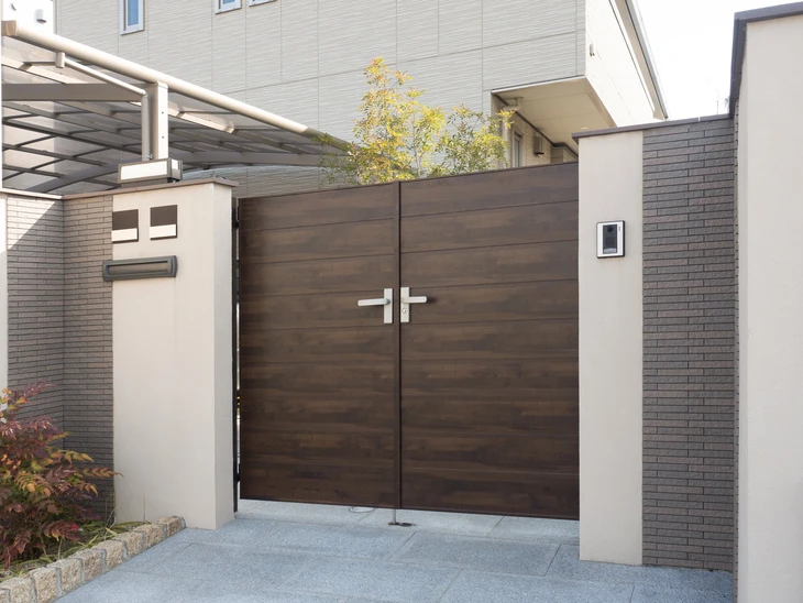 Entrée résidentielle moderne avec portail double battant en bois foncé, piliers en béton blanc et murs en briques grises