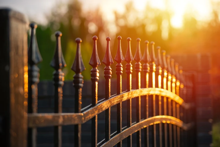 Clôture en fer forgé avec barreaux verticaux à pointes décoratives, photographiée en extérieur avec lumière dorée du soleil couchant