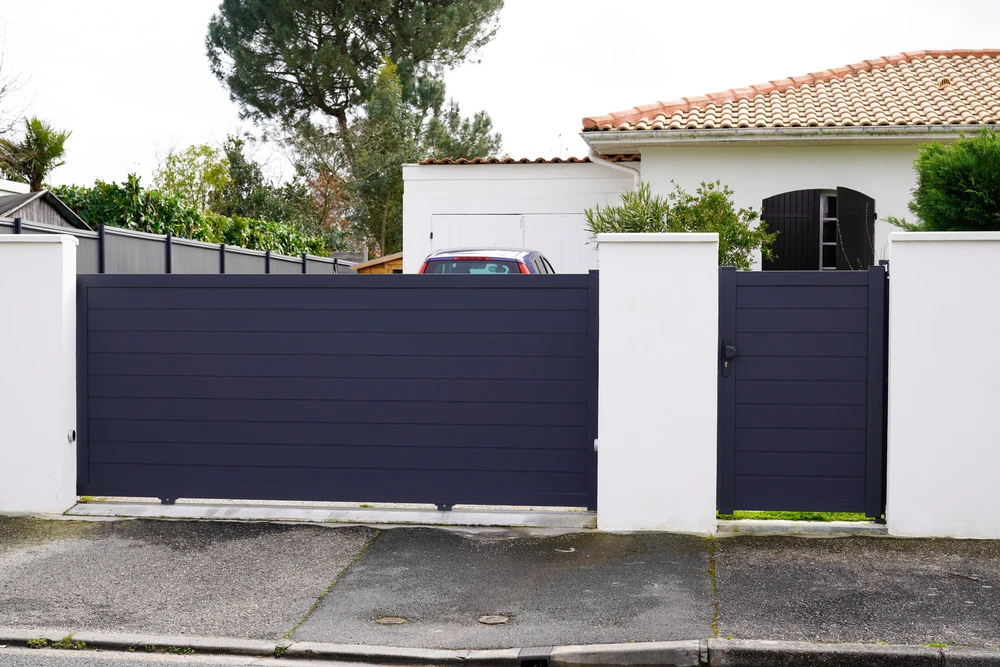 Entrée résidentielle moderne avec portail coulissant et portillon en aluminium anthracite, piliers en béton blanc