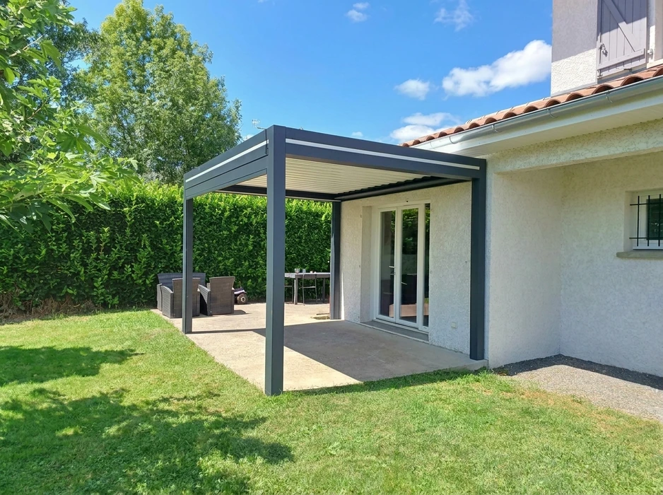 Terrasse extérieure couverte avec pergola en bois et colonnes blanches, aménagée d'un salon de jardin en résine tressée avec coussins gris sur plancher composite